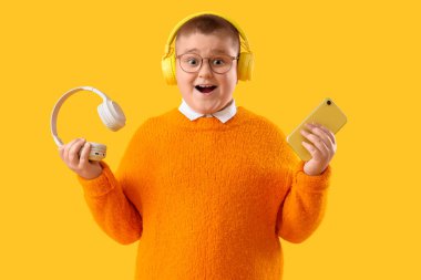 Sarı arka planda kulaklığı ve cep telefonu olan heyecanlı bir çocuk.