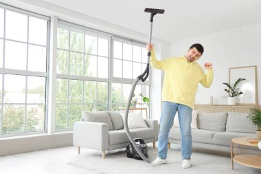 Halıyı süpüren ve odada müzik dinleyen genç bir adam.