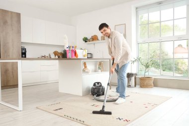 Genç adam mutfakta halı süpürüyor.