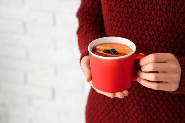 Beyaz tuğlalı arka planda sıcak şarap bardağı tutan kadın, yakın plan.