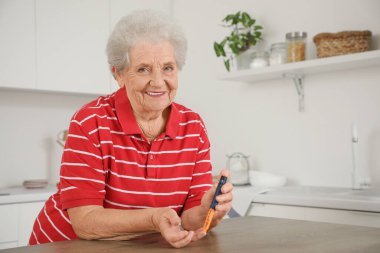 Diyabetik kıdemli kadın mutfaktaki masada tükenmez kalem kullanıyor.