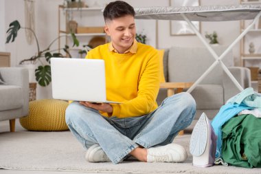 Bilgisayarı, ütüsü ve temiz giysileri olan yakışıklı genç adam evde oturuyor.