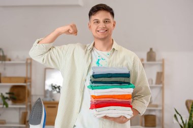 Evde kaslarını gösteren bir yığın temiz giysisi ve demiri olan yakışıklı genç adam.