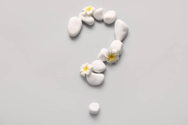 Gri arka planda spa taşlarından ve tropikal çiçeklerden oluşan soru işareti