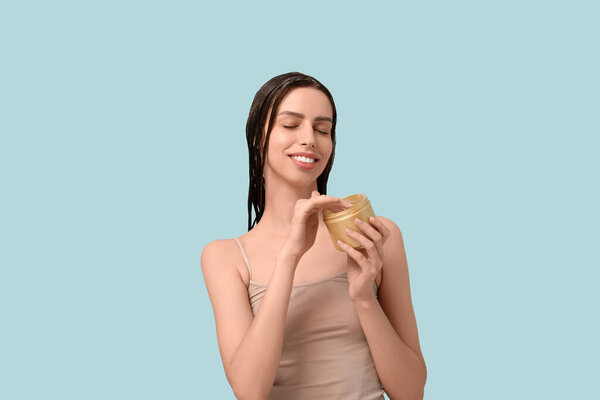 Красивая молодая счастливая женщина с баночкой маски для волос на синем фоне