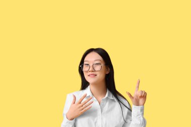 Güzel genç Asyalı kadın sarı arka plandaki bir şeyi işaret ediyor.