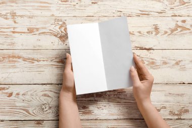Beyaz ahşap arka planda boş broşürleri olan kadın eller.