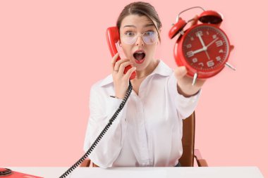 Alarmlı bir sekreter pembe arka planda telefonla konuşuyor.