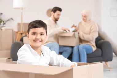 Mutlu Müslüman çocuk taşınma gününde karton kutuda oturuyor.