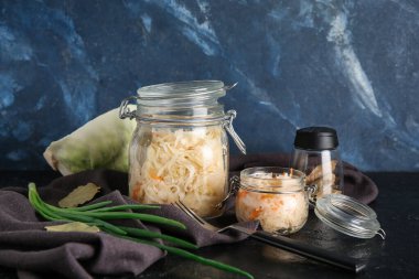 Mavi arka planda ev yapımı lahana turşusu, peçete ve yeşil soğanlı cam kavanoz. Yakın çekim.