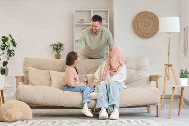 Müslüman ebeveynler ve kızları evdeki kanepede oturuyor.