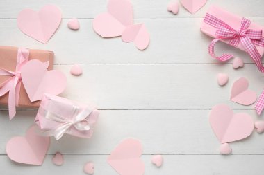 Beyaz tahta arka planda pembe kalpleri olan hediye kutularından yapılmış çerçeve. Sevgililer Günü kutlaması