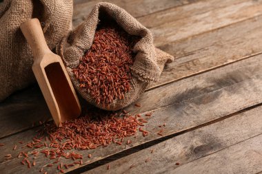 Tahta arka planda çiğ kahverengi pirinçli çuval ve kepçe.