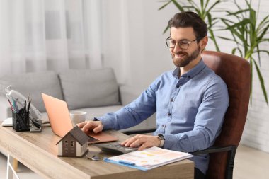 Masada çalışan hesap makinesi ve dizüstü bilgisayarı olan genç bir iş adamı.