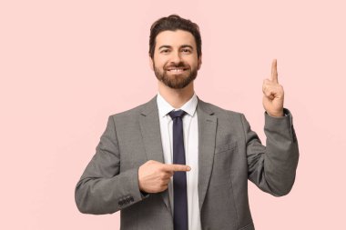 Genç işadamı pembe arka plandaki bir şeyi işaret ediyor.