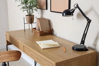 Ahşap masası, şık masa lambası ve evde kitapları olan modern çalışma alanı.