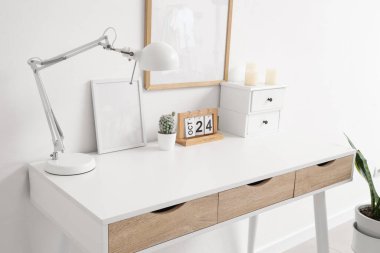 Masa lambası, takvimi ve beyaz duvarın yanında mumları olan modern masa.