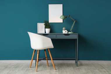 Rahat masalı modern çalışma alanı, şık masa lambası ve mavi duvarın yanındaki ev bitkisi.