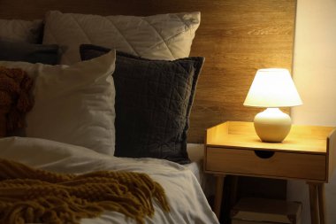 Şık bir yatak odası, rahat bir yatak odası ve gece yatağının yanında parlayan bir lamba.