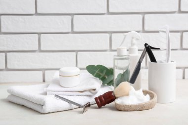 Beyaz tuğla duvarın yanındaki masada okaliptüs dallı tıraş aksesuarları.