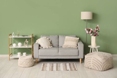 Rahat kanepe, raf ünitesi ve vazo. Oturma odasının iç kısmında çiçek açan manolya dalları var.