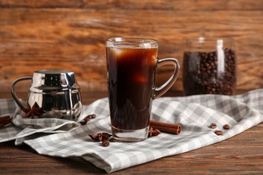 Tarçınlı bir bardak soğuk kahve ve ahşap zeminde bir sürahi taze süt.