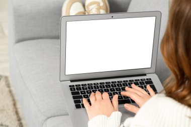 Evdeki kanepede boş dizüstü bilgisayar kullanan genç bir kadın.