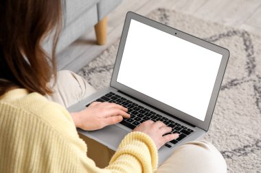 Evdeki kanepede boş dizüstü bilgisayar kullanan genç bir kadın.