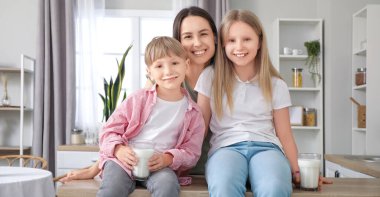 Bir bardak sütle iki kardeş ve anneleri mutfakta.