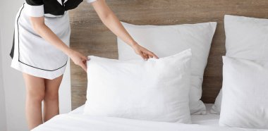 Oda hizmetçisi otel odasında yatak yapıyor.