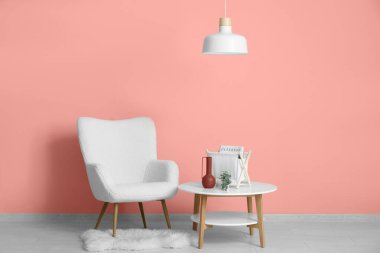 Beyaz koltuk, masa ve asılı lamba pembe duvarın yanında.