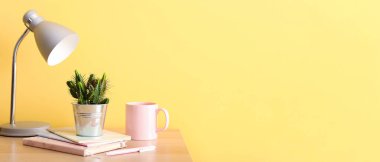 Yeşil kaktüs, defterler, lamba ve bardak sarı duvara karşı. Tasarım için pankart