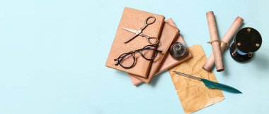 Eski kağıt çarşaf, kitaplar, tükenmez kalem, mürekkep hokkası, parşömenler ve açık mavi arkaplan üzerindeki gözlük.