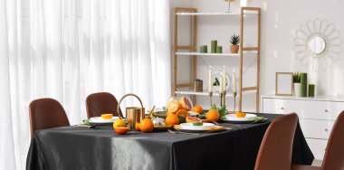 Narenciye meyveleri, yanan mumlar ve odada siyah masa örtüsü olan güzel bir masa.