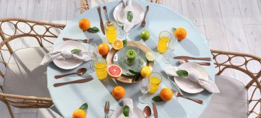 Narenciye meyveleri, yanan mum ve açık mavi masa örtüsü üzerine portakal suyu olan güzel bir masa.