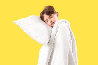 Sarı arka planda yastığı ve battaniyesi olan küçük uykulu bir çocuk.