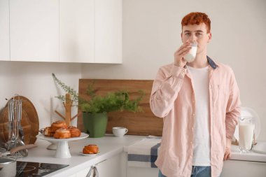 Genç kızıl adam mutfakta süt içiyor.