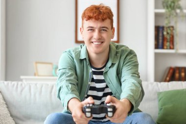 Genç kızıl saçlı adam evde video oyunu oynuyor.