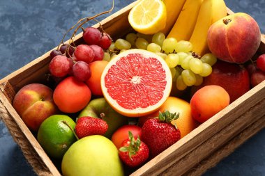 Mavi arka planda farklı taze meyveler olan tahta kutu.