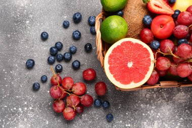 Gri masada farklı taze meyvelerle dolu sepet.