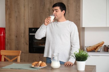 Genç adam mutfakta süt içiyor.