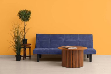 Kanepeli ahşap sehpa ve turuncu duvarın yanında bitkiler.