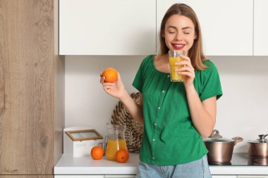 Mutfakta bir bardak meyve suyu ve portakal suyu olan genç bir kadın.