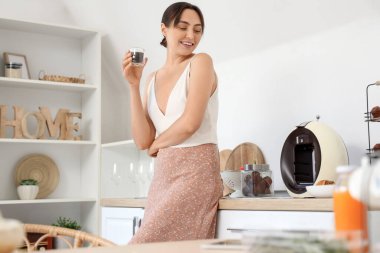 Genç ve güzel bir kadın mutfaktaki kahve makinesinin yanında sıcak espresso içiyor.