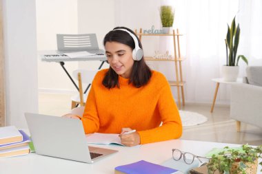 Kulaklıklı genç bir kadın evde İngilizce öğreniyor.