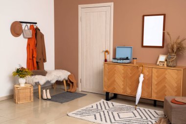 Modern koridorun içinde şık sonbahar kıyafetleri, bank ve ahşap büfe var.