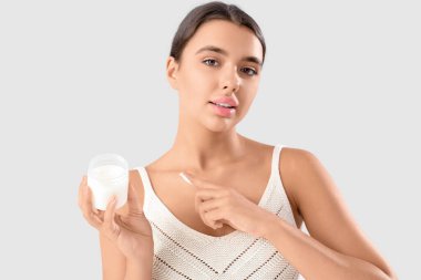 Gri arkaplana karşı vücuduna hindistan cevizi yağı süren güzel bir kadın.