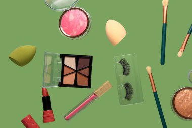 Yeşil arka planda uçan dekoratif kozmetik ürünleri