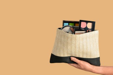 Sarı arka planda dekoratif kozmetik ürünleri olan bir çanta tutan kadın.