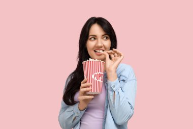 Pembe arka planda bir kova patlamış mısırı olan mutlu genç kadın.